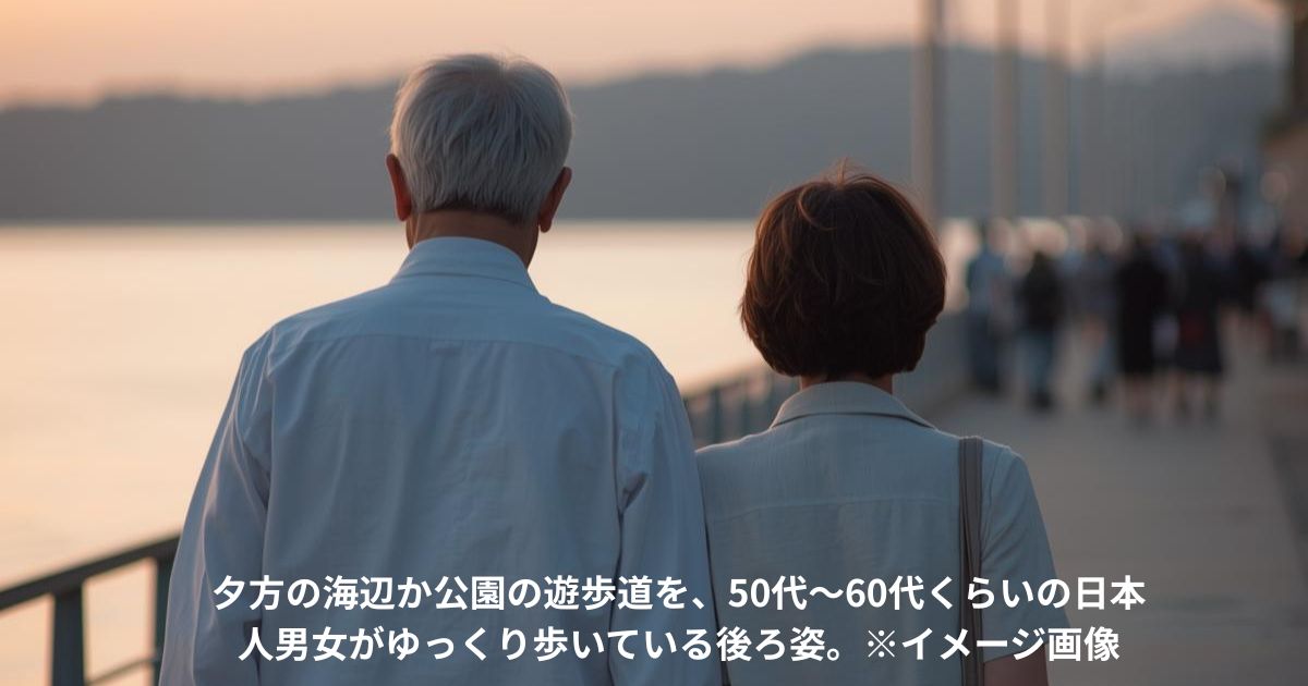夕方の海辺か公園の遊歩道を、50代〜60代くらいの日本人男女がゆっくり歩いている後ろ姿。
